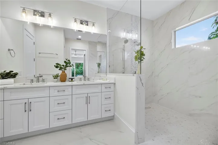 Full bath featuring a marble finish shower, light marble finish flooring, and double vanity