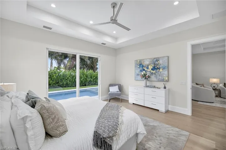 Bedroom with a tray ceiling, access to outside, light wood-style floors, a ceiling fan, and recessed lighting