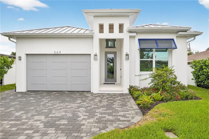 View of front facade with a standing seam roof, a metal roof, an attached garage, decorative driveway, and stucco siding