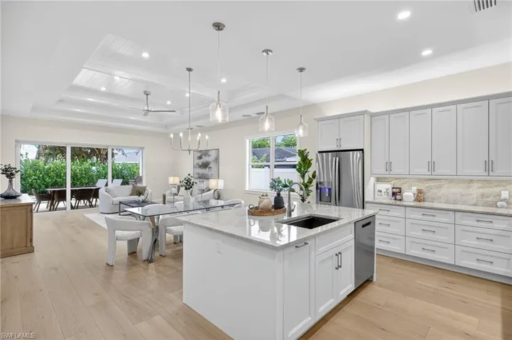 Kitchen featuring a raised ceiling, open floor plan, hanging light fixtures, appliances with stainless steel finishes, and light stone countertops