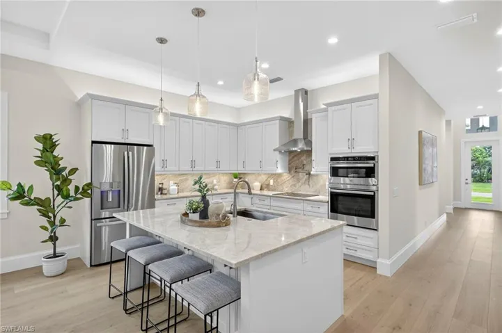 Kitchen with appliances with stainless steel finishes, light stone counters, a kitchen breakfast bar, decorative light fixtures, and tasteful backsplash