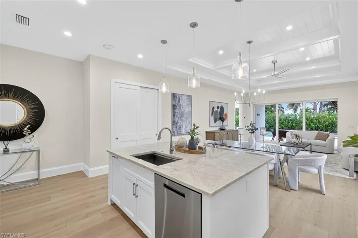 Kitchen featuring white cabinetry, light stone counters, stainless steel dishwasher, light wood finished floors, and a raised ceiling
