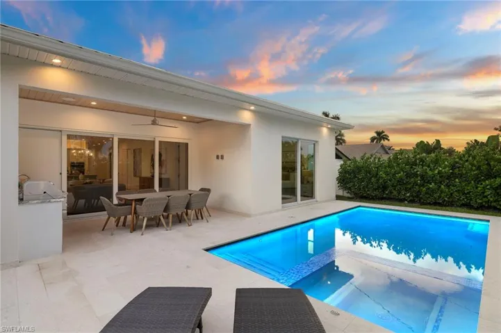 Pool at dusk featuring a pool with connected hot tub, ceiling fan, a patio area, and outdoor dining space
