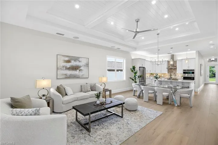 Living area with a ceiling fan, light wood-style floors, recessed lighting, a chandelier, and a tray ceiling