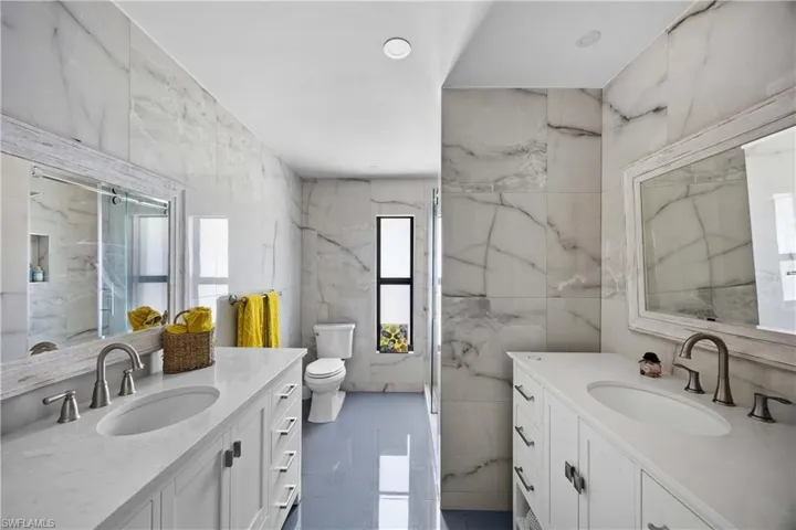 Bathroom featuring two vanities, tile walls, recessed lighting, and a marble finish shower