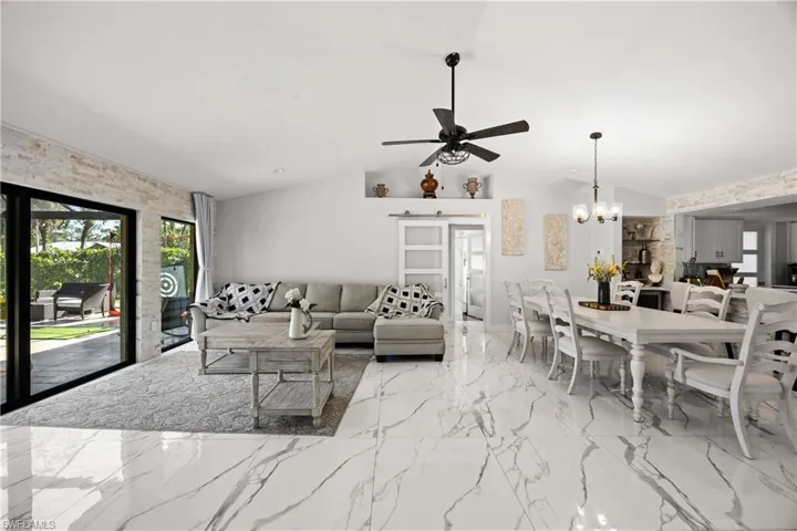 Living room with a barn door, light marble finish flooring, ceiling fan, lofted ceiling, and a chandelier