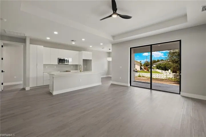 Unfurnished living room with a tray ceiling, ceiling fan, dark wood-style floors, and recessed lighting