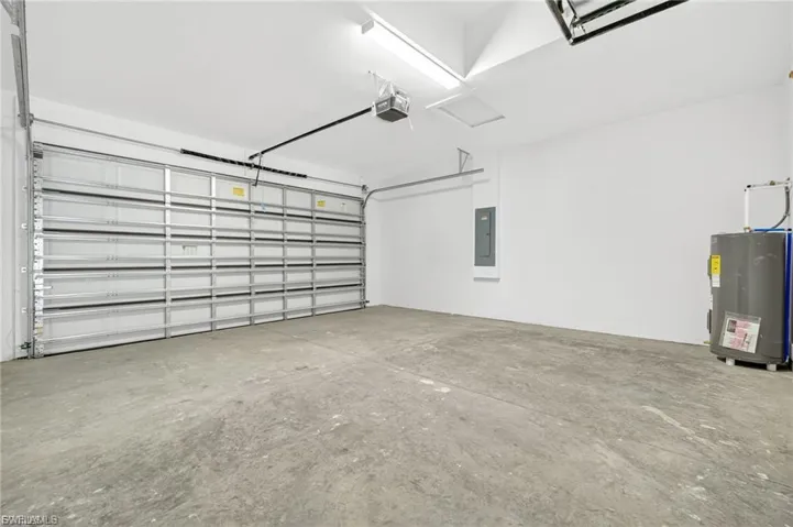 Garage with electric water heater, electric panel, and a garage door opener