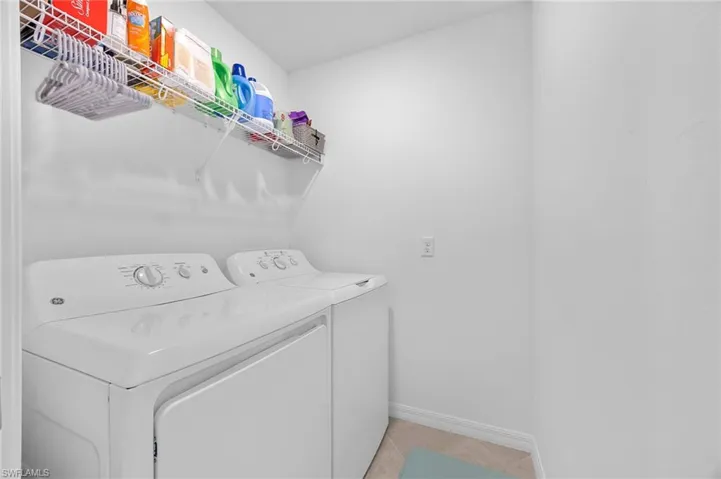 Washroom with washing machine and dryer and light tile patterned floors