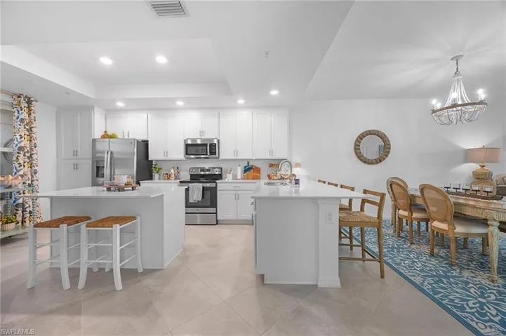 Kitchen with a kitchen bar, a chandelier, a peninsula, a raised ceiling, and recessed lighting