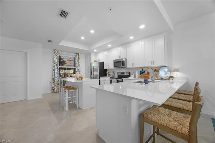 Kitchen with a breakfast bar area, a peninsula, a kitchen island, a tray ceiling, and appliances with stainless steel finishes