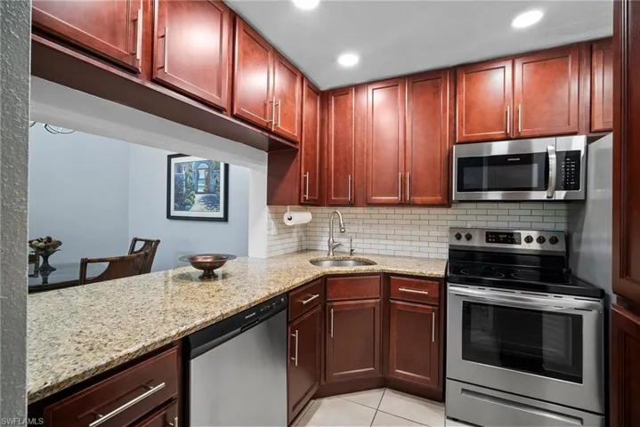 Kitchen featuring stainless steel appliances, light stone counters, sink, tasteful backsplash, and light tile patterned floors