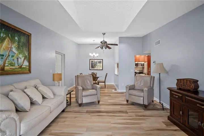 Living room with light wood-type flooring, a textured ceiling, and ceiling fan with notable chandelier