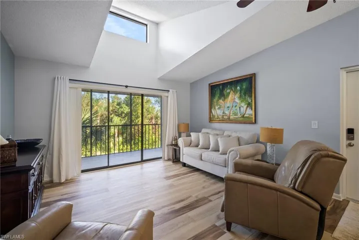 Living room featuring ceiling fan, a textured ceiling, light wood-type flooring, and lofted ceiling