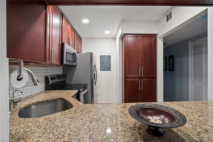 Kitchen with electric panel, light stone counters, backsplash, appliances with stainless steel finishes, and sink