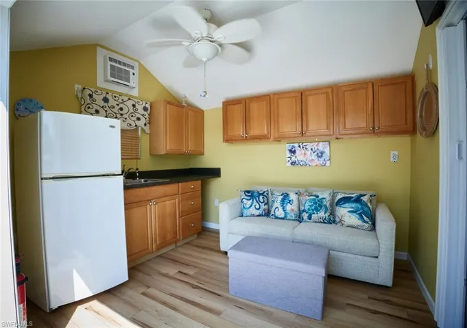 Kitchen featuring lofted ceiling, sink, light hardwood / wood-style flooring, a wall unit AC, and white refrigerator