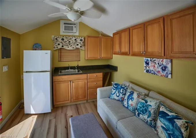 Kitchen with sink, electric panel, white fridge, an AC wall unit, and light wood-type flooring