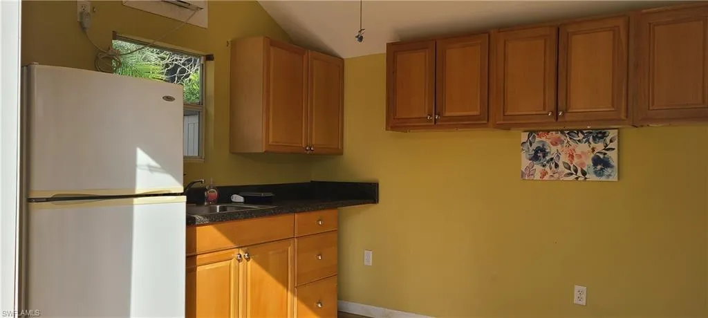 Kitchen featuring brown cabinets, a sink, freestanding refrigerator, and dark countertops