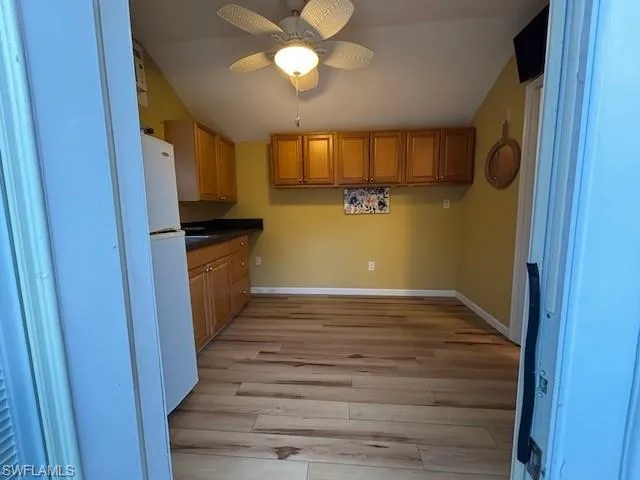 Kitchen with ceiling fan, freestanding refrigerator, dark countertops, light wood finished floors, and baseboards