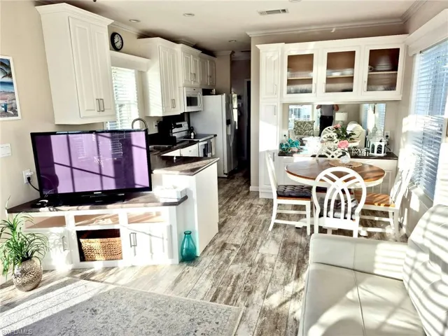 Kitchen/Dining featuring modern cabinets crown molding, range with newer appliances,  glass insert cabinets, white cabinetry, and light wood-style floors