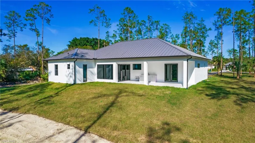 Rear view of house with stucco siding, a yard, a patio, and a metal roof