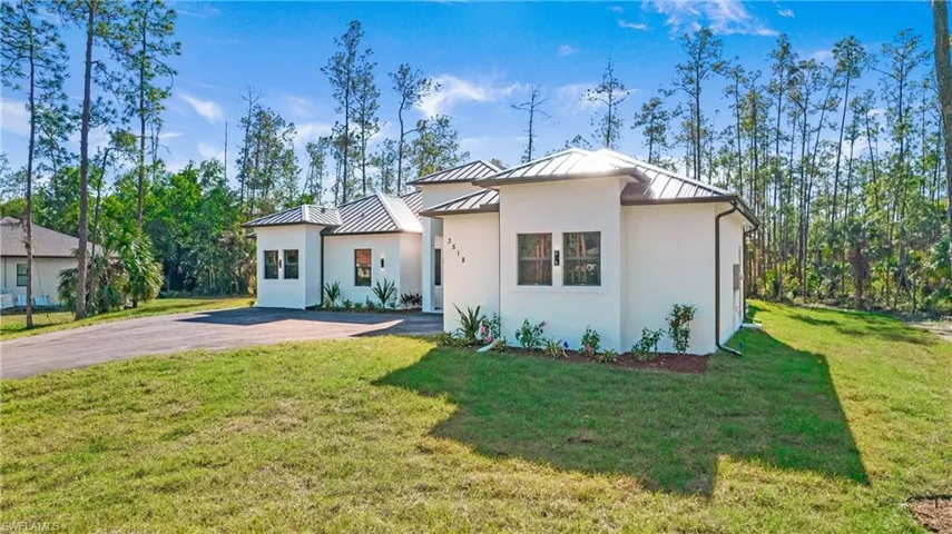 Modern home with a standing seam roof, a front lawn, stucco siding, and asphalt driveway