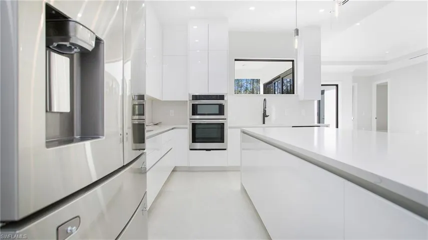 Kitchen featuring stainless steel appliances, modern cabinets, white cabinets, decorative light fixtures, and light stone counters