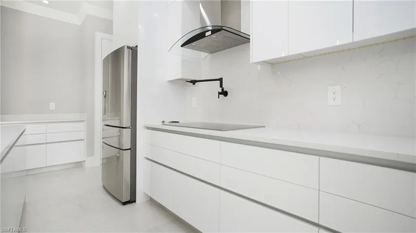 Kitchen featuring modern cabinets, white cabinetry, exhaust hood, stainless steel fridge, and ornamental molding