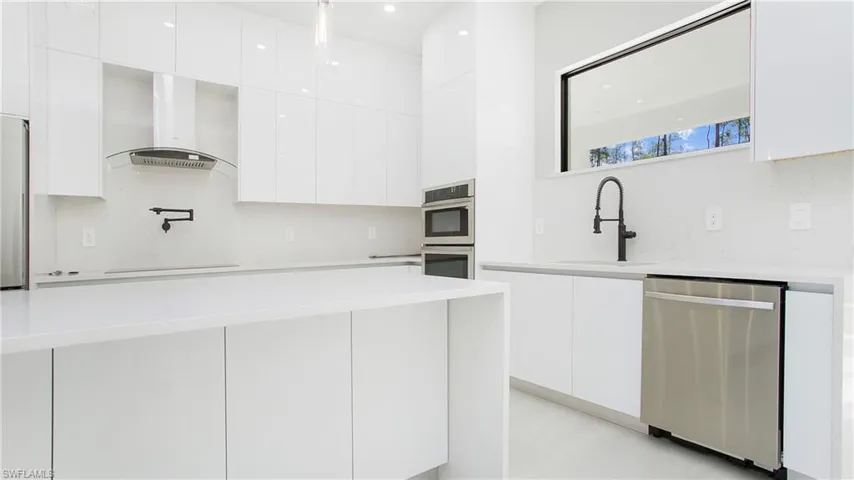 Kitchen with modern cabinets, stainless steel appliances, white cabinetry, and light stone counters