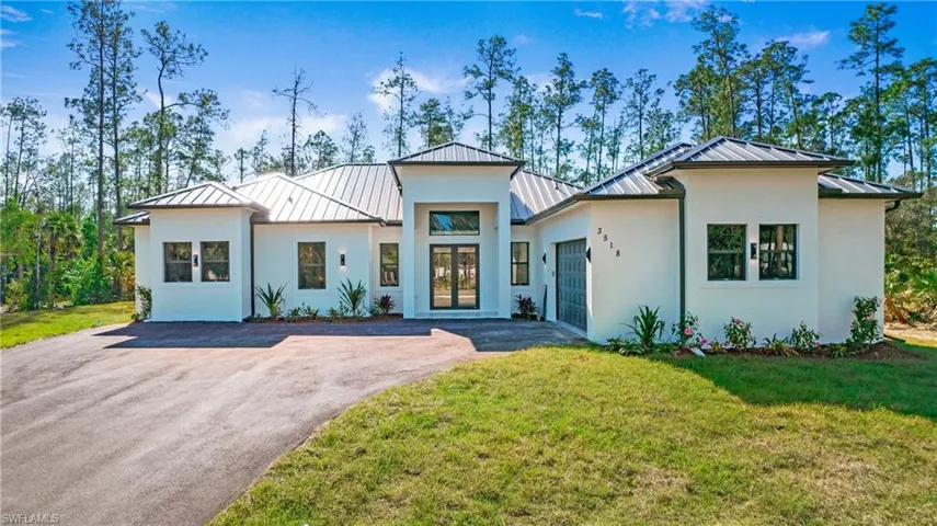 Contemporary home featuring a standing seam roof, an attached garage, driveway, and a front lawn