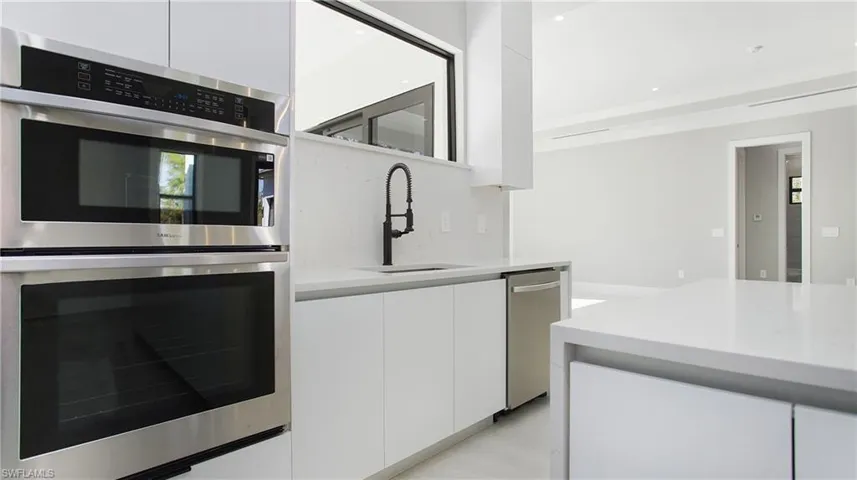 Kitchen with stainless steel appliances, modern cabinets, white cabinets, and light stone counters