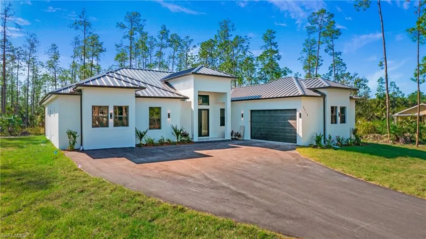 View of front of home featuring a standing seam roof, a front yard, asphalt driveway, and a garage