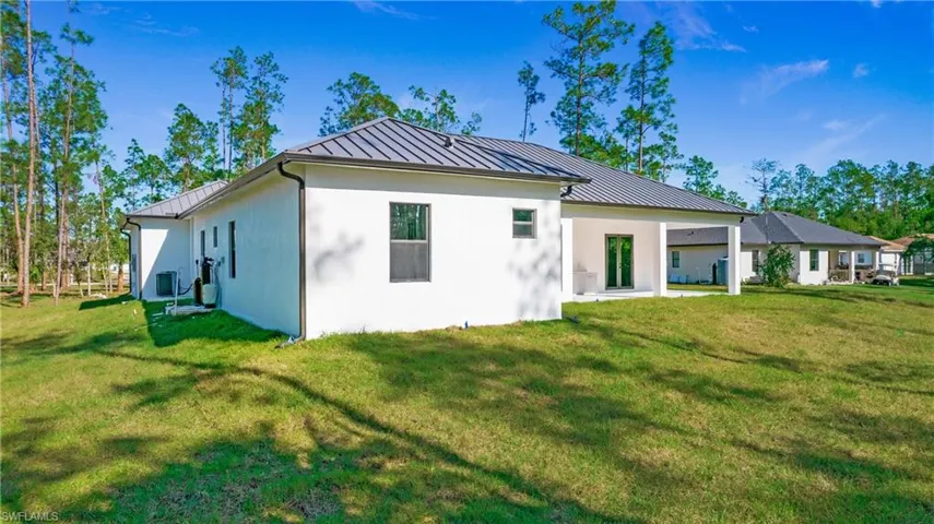Rear view of property featuring a standing seam roof, a yard, a patio area, and stucco siding