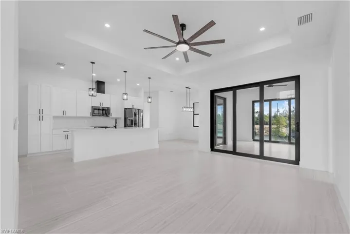 Unfurnished living room featuring ceiling fan, recessed lighting, and a tray ceiling