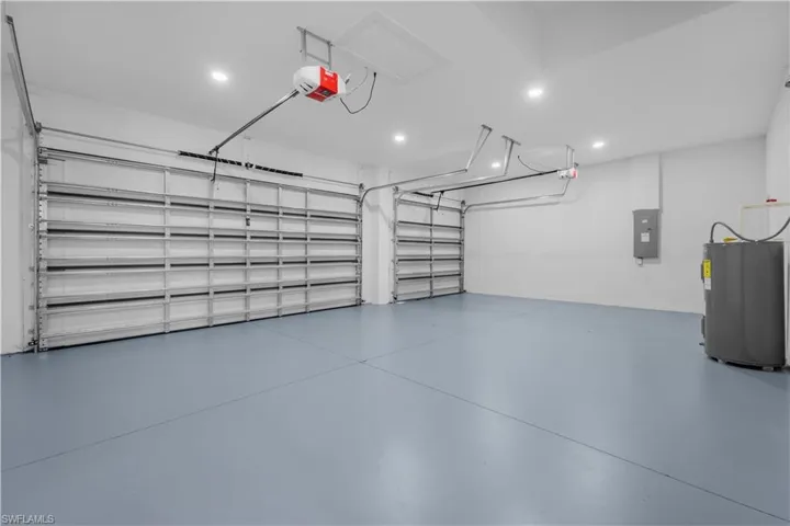 Garage with water heater, a garage door opener, electric panel, and recessed lighting