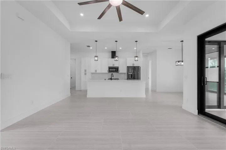 Unfurnished living room featuring a tray ceiling, ceiling fan, and recessed lighting