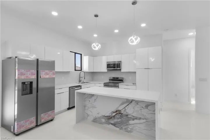 Kitchen with stainless steel appliances, modern cabinets, light stone counters, white cabinets, and hanging light fixtures