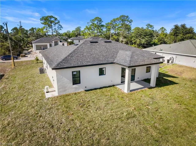 Rear view of house with a shingled roof, stucco siding, and a yard