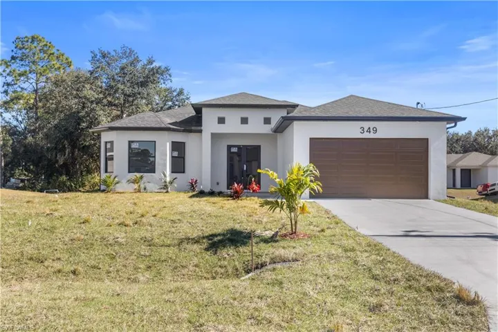 Prairie-style house featuring stucco siding, a shingled roof, a front lawn, concrete driveway, and a garage