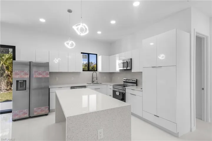 Kitchen with hanging light fixtures, stainless steel appliances, modern cabinets, white cabinets, and a kitchen island