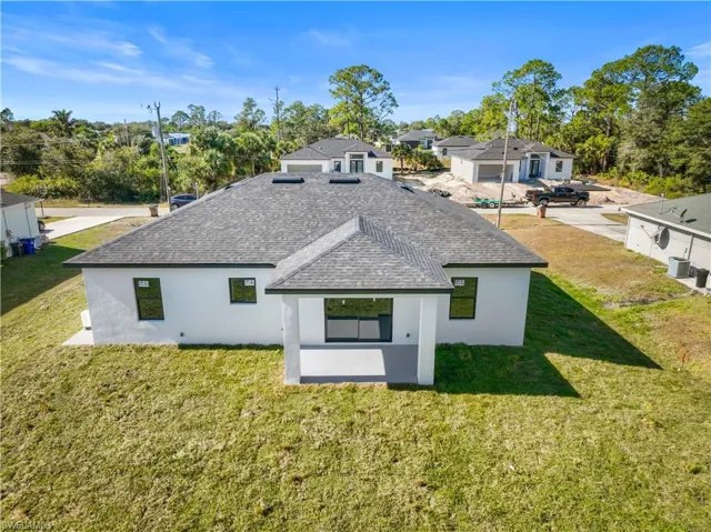 Rear view of house with a shingled roof, stucco siding, a lawn, and a patio area