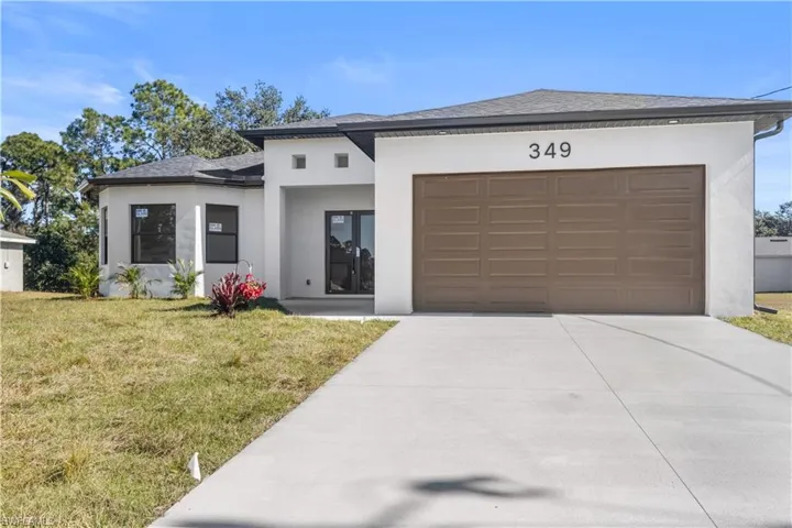 View of front of house featuring stucco siding, roof with shingles, concrete driveway, and a front yard