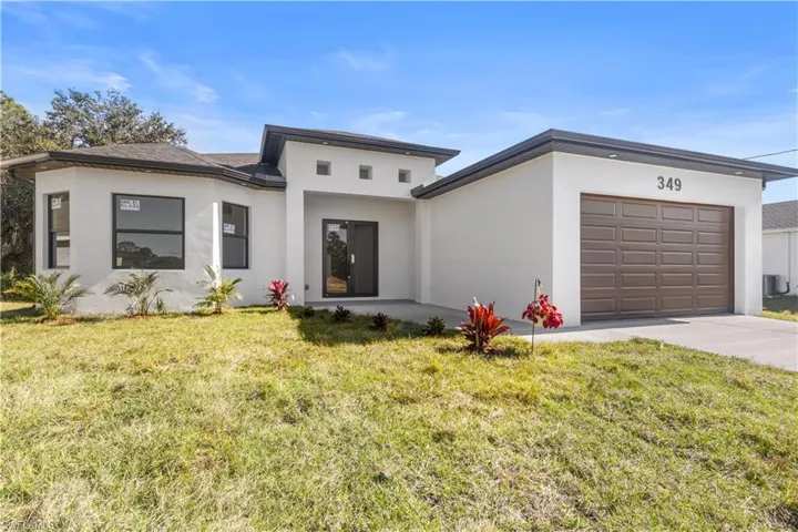 View of front facade featuring an attached garage, a front yard, stucco siding, and driveway
