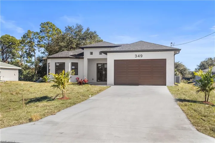 View of front facade featuring stucco siding, driveway, roof with shingles, and a front lawn