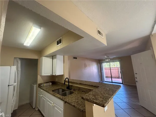 Kitchen featuring freestanding refrigerator, light tile patterned floors, white cabinetry, a peninsula, and a textured ceiling