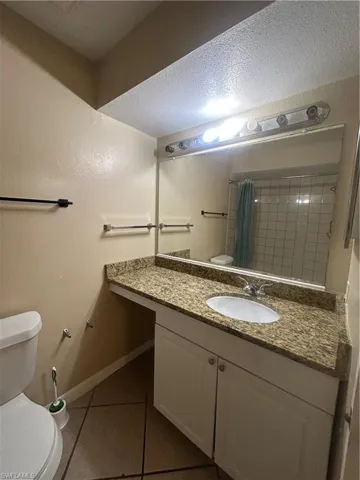 Full bath featuring dark tile patterned floors, a textured ceiling, vanity, and curtained shower