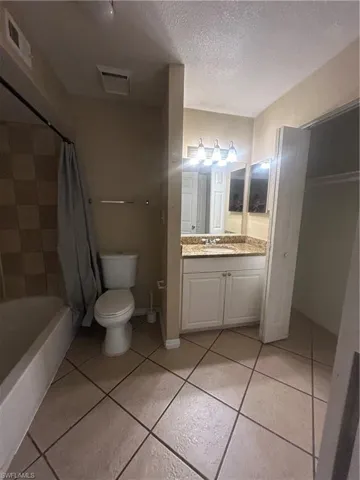 Bathroom with vanity, a textured ceiling, shower / tub combo with curtain, and light tile patterned flooring
