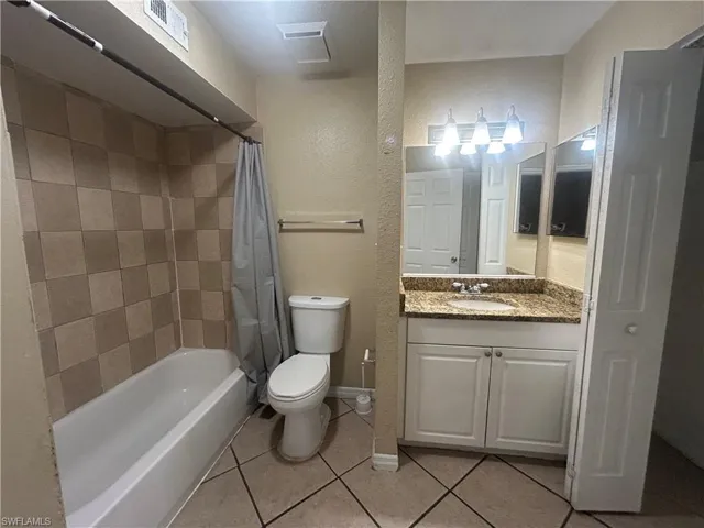 Bathroom featuring a textured wall, shower / tub combo, vanity, and light tile patterned flooring