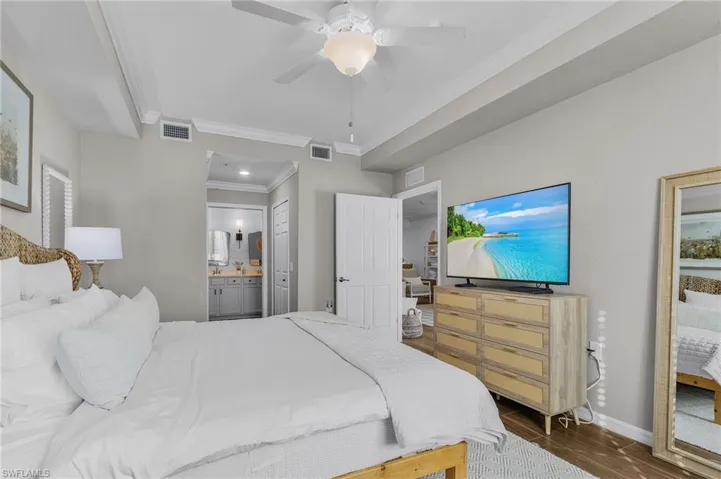 Bedroom with ensuite bathroom, ceiling fan, ornamental molding, and dark wood-type flooring