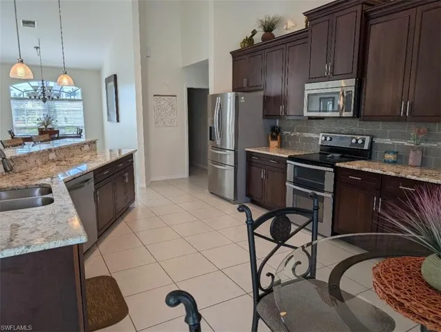 Kitchen featuring stainless steel appliances, a sink, baseboards, tasteful backsplash, and dark brown cabinets